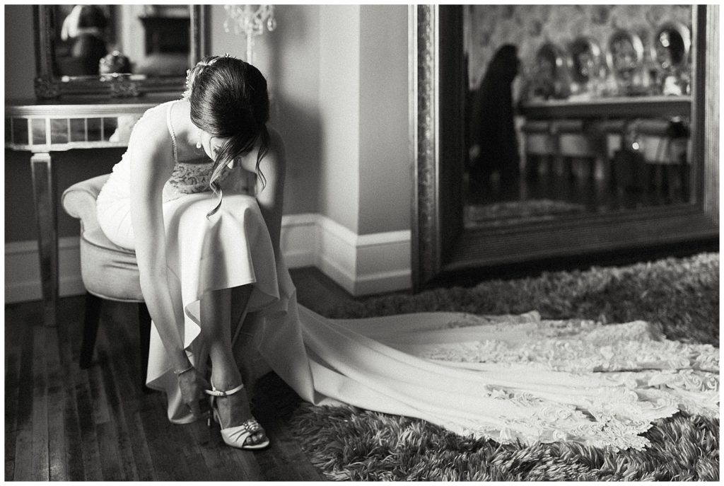 Bride buckles her shoe in a tidy getting ready space which gives her the best wedding getting ready photos.
