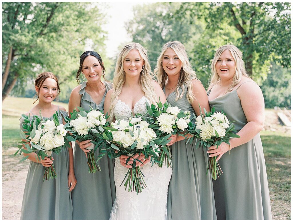 Bride and bridesmaids with ivory wedding bouquets and green dresses.