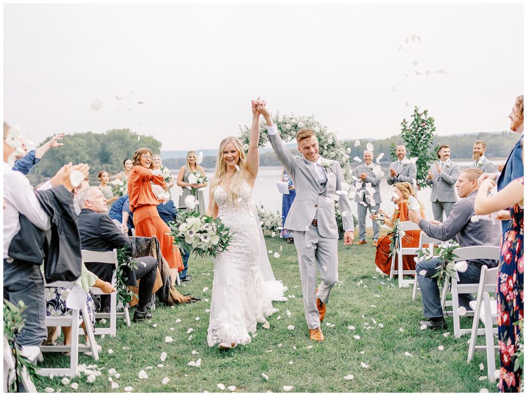 Bride and groom recess down the aisle as guests toss rose pedals.