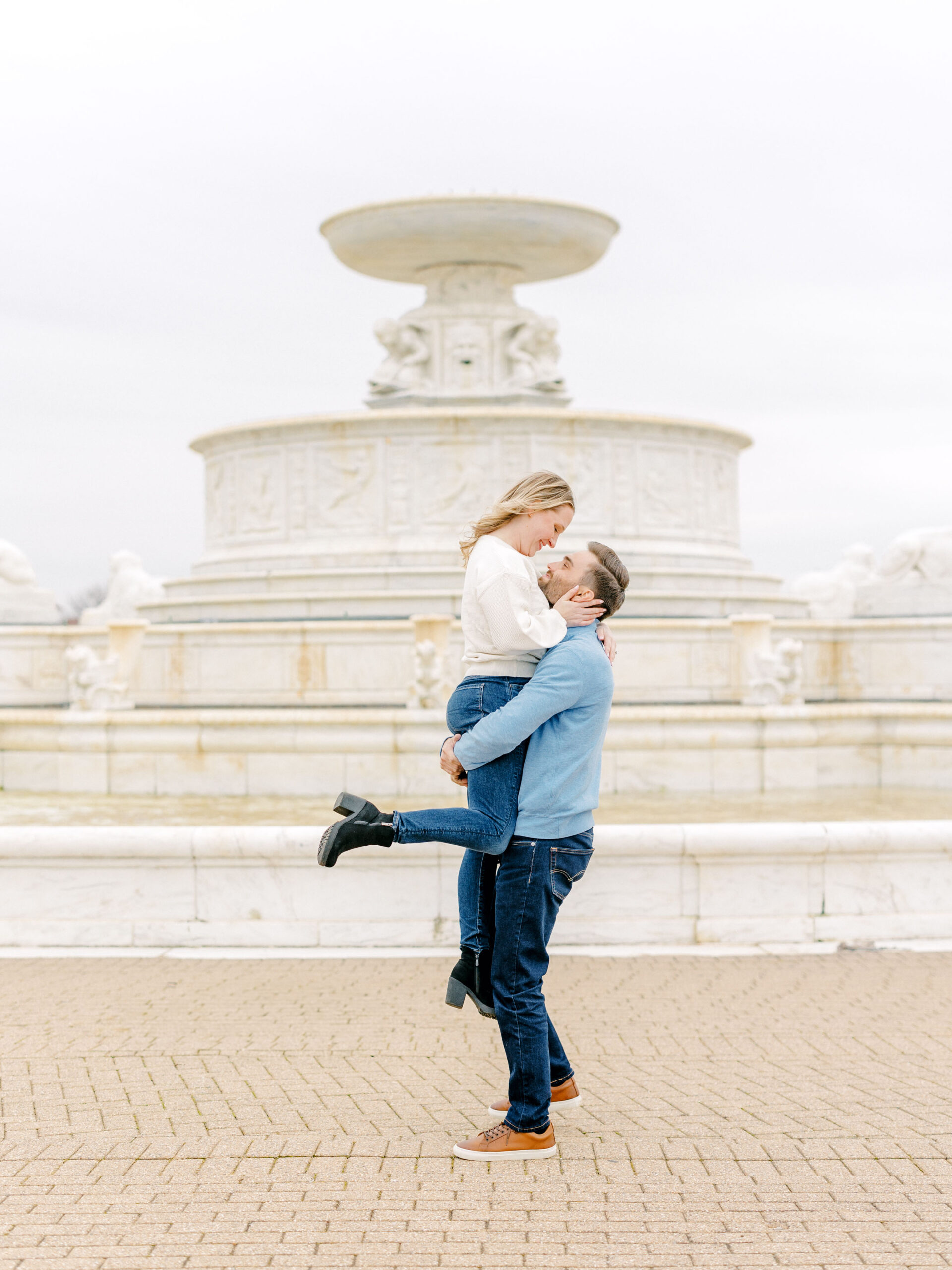 Brunette guy lifts girl blonde girl in front of fountain